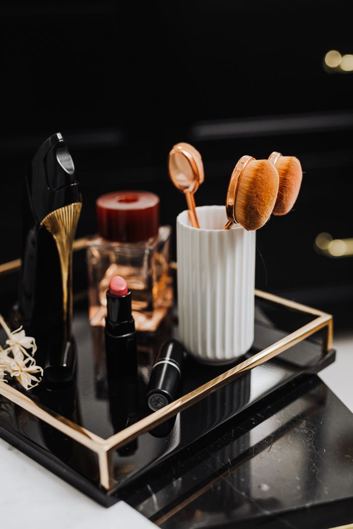 Home A stylish display of makeup and beauty tools including lipstick, brushes, and perfume on a black tray.